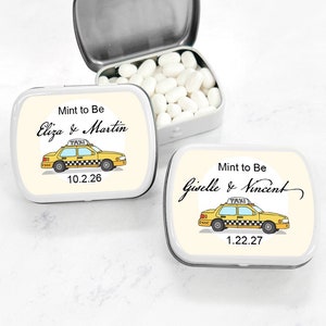 May include: Two yellow and black taxi cab themed mint tins with the text "Mint to Be" and the names of the couples getting married. The first tin says "Eliza & Martin" and the date "10.2.26". The second tin says "Giselle & Vincent" and the date "1.22.27".