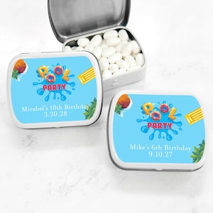 May include: Two small, white, rectangular tins with blue lids. The tins are decorated with a cartoon image of a pool party with the words "Pool Party" in red and yellow letters. The text on the tins reads "Mirabel's 10th Birthday 3.20.28" and "Mike's 6th Birthday 9.10.27".