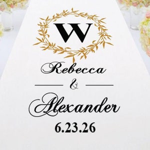 May include: White wedding aisle runner with a gold wreath and the letter W in the center. The text "Rebecca & Alexander 6.23.26" is printed below the wreath.