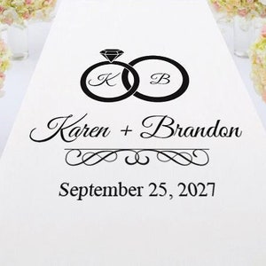 May include: White aisle runner with black text and a graphic of two interlocking rings with a diamond. The text reads "Karen + Brandon" and "September 25, 2027".