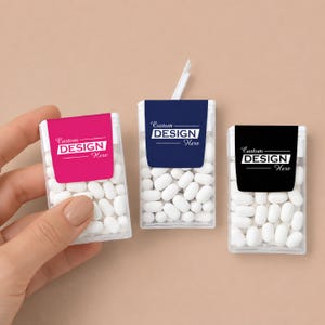 May include: Three clear rectangular plastic containers filled with small white oval mints. Each container features a label with the text Custom DESIGN Here in pink, navy blue, or black. One container has a white plastic tab extending from the top.
