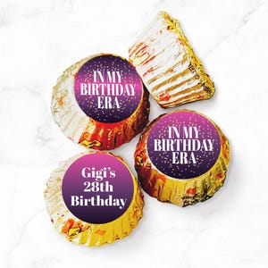 May include: Four chocolate candies wrapped in gold foil with purple and pink gradient labels. The labels have white text that reads "In my birthday era" and "Gigi's 28th Birthday".