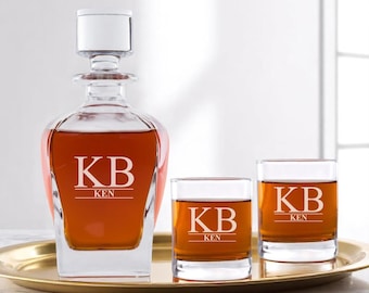 May include: A personalized whiskey decanter set with two glasses, filled with amber liquid, and a gold tray. The decanter and glasses are engraved with the initials "KB" and the name "KEN". The set is displayed on a gold tray.