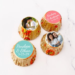 May include: Four personalized chocolate favors with photos and names. The favors are wrapped in gold foil with a red and orange design. The names and dates are printed on the favors in white text. The favors are arranged on a white surface.