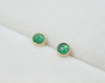 May include: A pair of emerald green gemstone earrings with gold settings.