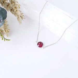 May include: A silver chain necklace with a single, round, dark red gemstone pendant.