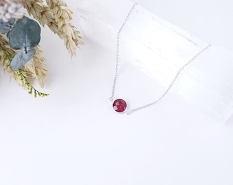 May include: A silver chain necklace with a single, round, dark red gemstone pendant.