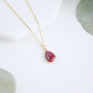 May include: A gold chain necklace with a teardrop-shaped pendant featuring a red gemstone.