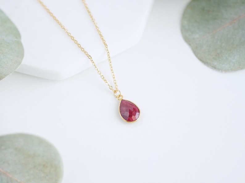 May include: A gold chain necklace with a teardrop-shaped pendant featuring a red gemstone.