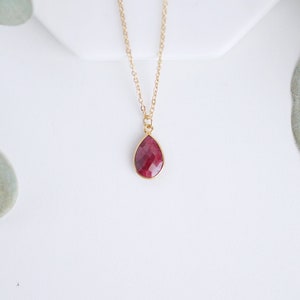 May include: A gold chain necklace with a teardrop-shaped pendant featuring a red gemstone.