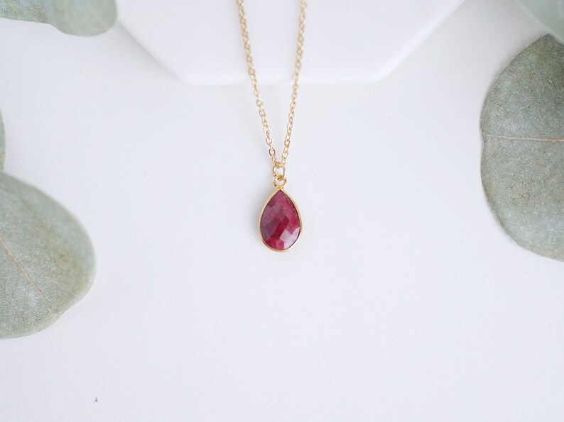 May include: A gold chain necklace with a teardrop-shaped pendant featuring a red gemstone.