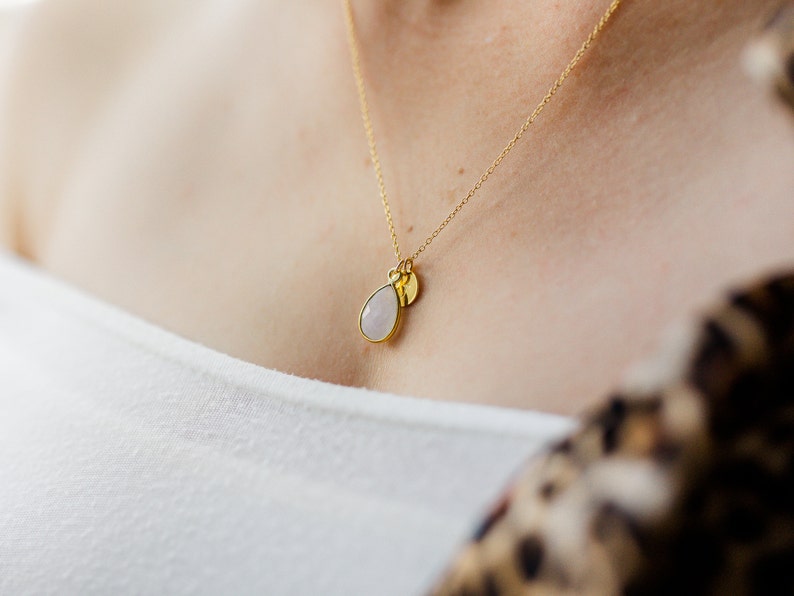 May include: A gold chain necklace with a teardrop-shaped white stone pendant and a small gold disc pendant.