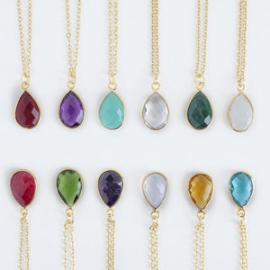 May include: A set of 12 gold necklaces with teardrop-shaped gemstone pendants. The gemstones are in various colours, including red, purple, blue, green, and clear.