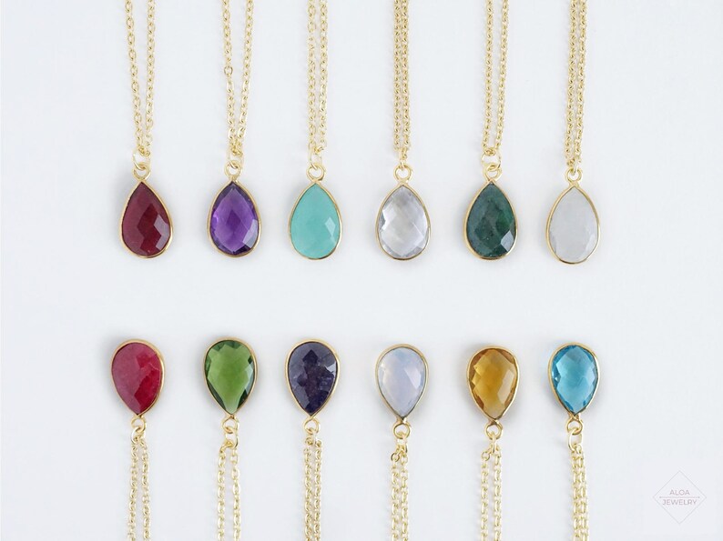 May include: A set of 12 gold necklaces with teardrop-shaped gemstone pendants. The gemstones are in various colours, including red, purple, blue, green, and clear.