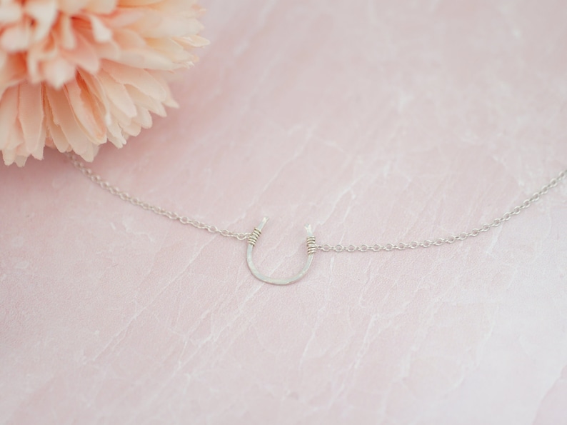 Puede incluir: Un collar de plata en forma de herradura con una cadena delicada. La herradura est&aacute; martillada y tiene un acabado ligeramente texturizado.