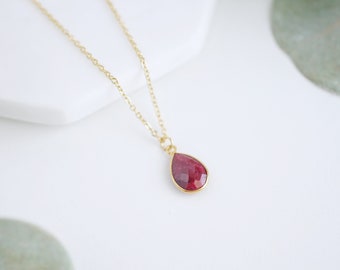 May include: A delicate gold chain necklace with a teardrop-shaped ruby pendant.