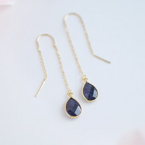 May include: A pair of gold dangle earrings with teardrop-shaped blue gemstone accents.