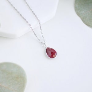 May include: A silver chain necklace with a teardrop-shaped pendant featuring a deep red gemstone.