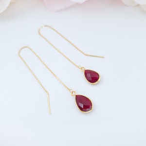 May include: A pair of gold dangle earrings with red teardrop-shaped gemstones.