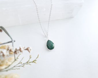 May include: A silver chain necklace with a teardrop-shaped green gemstone pendant.