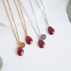 May include: Three gold and silver necklaces with red gemstone teardrop pendants and initial charms.