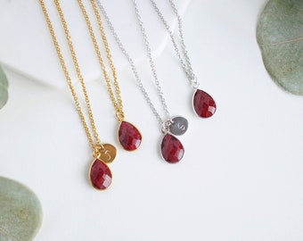 May include: Three gold and silver necklaces with red gemstone teardrop pendants and initial charms.