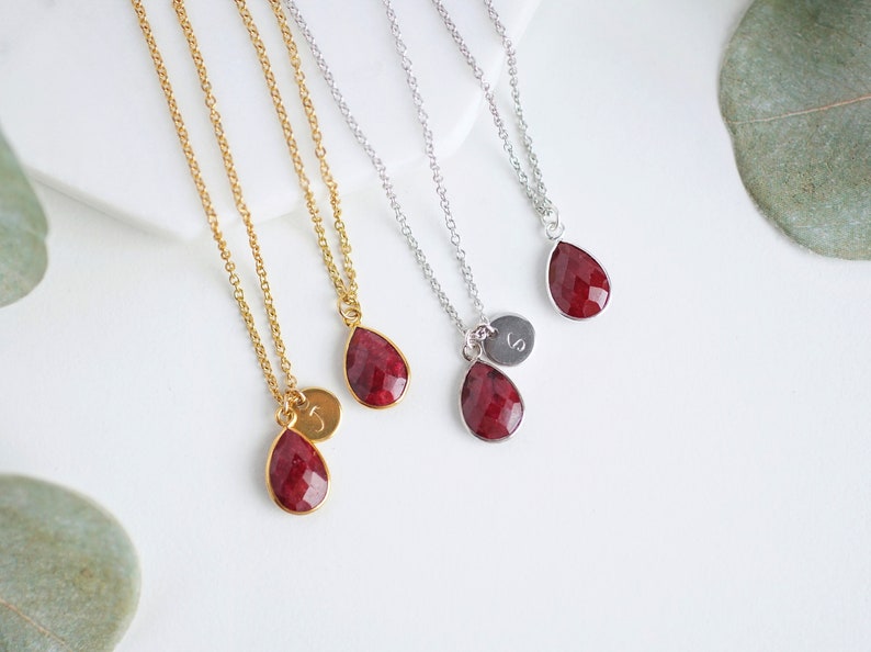 May include: Three gold and silver necklaces with red gemstone teardrop pendants and initial charms.