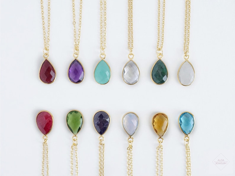 May include: A set of 12 gold necklaces with teardrop-shaped gemstone pendants. The gemstones are in various colors, including red, purple, blue, green, and clear.