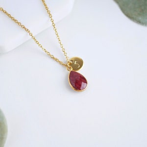 May include: A gold chain necklace with a teardrop-shaped red gemstone pendant and a small gold disc charm with the number "5" engraved on it.