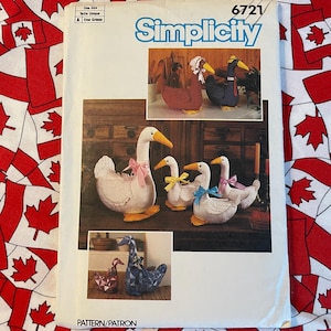 May include: Simplicity pattern 6721 showing images of stuffed goose and duck figures. The cover displays various goose and duck designs with bows. The background is a red and white Canadian flag pattern.