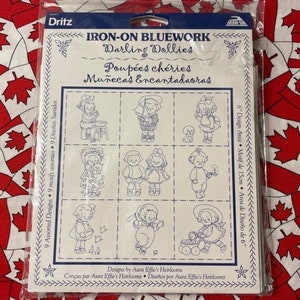 May include: A sheet of iron-on bluework designs featuring nine darling dollies. Each design is approximately 15cm in size. The designs are titled "Darling Dollies" and are available in English, French, and Spanish.