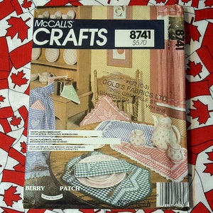 Peut inclure: Un patron de couture McCall's Crafts pour un ensemble de cuisine sur le thème de la fraise. Le patron comprend des instructions pour la réalisation d'une nappe, de serviettes, de sets de table et d'un dessous de plat. Le patron est imprimé sur un fond blanc avec du texte rouge et bleu. Le numéro du patron est 8741 et le prix est de 5,70 $.