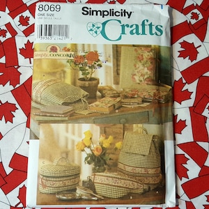 May include: Simplicity Crafts sewing pattern number 8069, one size, for making a set of four storage boxes. The pattern shows a floral fabric with a gingham trim. The boxes are shown on a table with a floral fabric tablecloth.