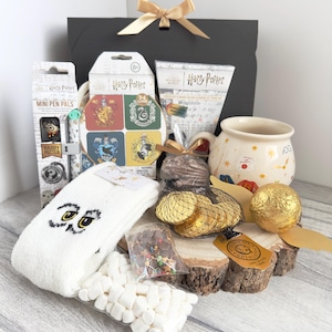 May include: A Harry Potter themed gift basket containing a mug, socks, chocolate coins, marshmallows, hot chocolate mix, and other Harry Potter themed items.