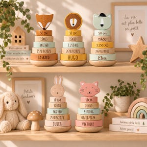 Peut inclure: Cinq jouets à empiler en bois avec des têtes d'animaux : renard, lion, ours, lapin et chat. Chaque jouet comporte des anneaux empilés imprimés avec des détails de naissance comme 50 cm, l'heure, le poids en kg, la date et les prénoms des enfants.