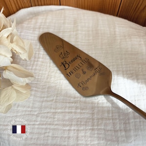 Peut inclure: Un serveur à gâteau en argent gravé avec le texte "Les Bonnes Tartelettes de Mamounite". Le serveur est décoré de petits dessins de pâtisseries.