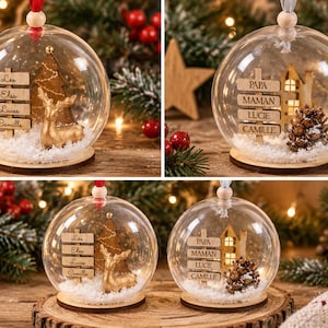 Peut inclure: Boules de No&euml;l transparentes contenant des panneaux en bois grav&eacute;s avec des pr&eacute;noms. L'une contient un cerf et un sapin dor&eacute;s, l'autre une petite maison et une pomme de pin, le tout pos&eacute; sur une base de neige artificielle.