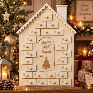 Peut inclure: Un calendrier de l'Avent en bois en forme de maison avec vingt-quatre petits tiroirs, chacun doté d'un bouton rond et d'un numéro imprimé. La porte centrale est gravée du texte Joyeux Noël Sarah et d'un sapin, en bois clair.