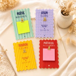 Peut inclure: Quatre porte-mémo colorés aux bords festonnés. Chaque support a une couleur et un design différents, avec du texte et une petite pince retenant un post-it carré. Le texte comprend des noms et des phrases comme "Merci pour cette belle année."