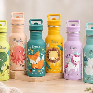 Op de afbeelding: Zes kleurrijke metalen drinkflessen met draaghengsels en doppen. Elke fles heeft een unieke dierenillustratie en een naam: Nathan met een dinosaurus, Paola met een octopus, Emma met een vos, Jules met een leeuw, Nina met een eenhoorn en Paul met een ijsbeer. De merknaam Sassi staat op elke fles.