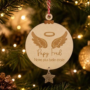 Peut inclure: Une décoration de Noël ronde en bois gravée d'ailes d'ange et d'une auréole. Le texte "Papy Fred" et "Notre plus belle étoile" est inscrit au centre. Une petite étoile dorée texturée est suspendue à la base de l'ornement.