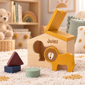 Peut inclure: Un jouet de tri de formes en bois en forme de maison avec un toit à charnière, portant le nom Jules imprimé sur le devant. Une pièce jaune en forme de lion est placée devant la maison, avec un triangle rouge foncé, un carré bleu et un cylindre vert sauge.