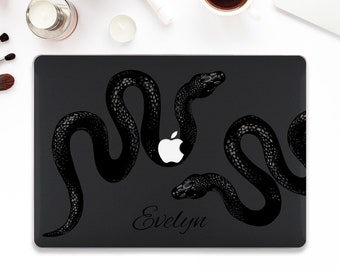 May include: Black laptop skin with a design of two snakes intertwined. The snakes are black and the background is a dark gray. The Apple logo is visible in the center of the skin. The text "Evelyn" is printed in white at the bottom of the skin.