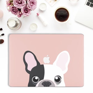 May include: A pink laptop skin featuring a black and white French bulldog peeking out from the bottom. The bulldog has a pink nose and black eyes. The Apple logo is visible on the laptop.