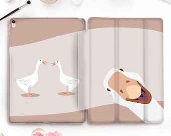 Puede incluir: Una funda para iPad rosa y blanca con un diseño de dos gansos blancos que se miran y un ganso blanco que asoma por la parte inferior de la funda. La funda está hecha de un material transparente y flexible.