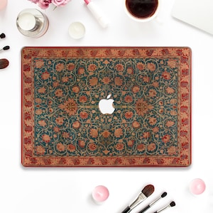 Op de afbeelding: Een laptop met een decoratieve hoes met een vintage bloemenpatroon in tinten rood, groen en goud. De hoes heeft een rode rand en een wit Apple-logo in het midden.