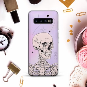 May include: A lavender phone case featuring a detailed illustration of a human skull and rib cage. The design includes stars, hearts, and a line art style. The case is surrounded by other objects.
