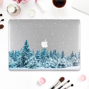 May include: A silver laptop with a wintery forest scene on the cover. The scene features a snowy forest with blue pine trees and a white background with white snowflakes.