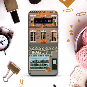 May include: A phone case featuring a bookstore design. The case depicts a brick building with windows, autumn leaves, and a black cat. The bookstore has a sign and pumpkins. The case is designed for a smartphone.