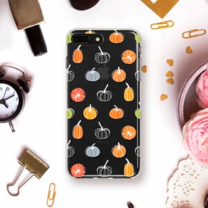 May include: A clear iPhone case with a black background, featuring a pattern of colorful pumpkins in orange, yellow, gray, and white. The case is designed for an iPhone and has the Apple logo visible.